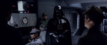 Movie still from “Star Wars: Episode V - The Empire Strikes Back” (1980), directed by Irvin Kershner – A man in a darth vader costume standing in front of other men; Medium shot, Over the shoulder angle
