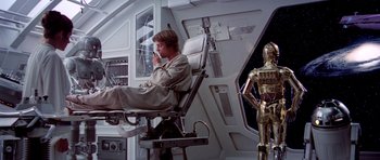 Movie still from “Star Wars: Episode V - The Empire Strikes Back” (1980), directed by Irvin Kershner – A man sitting in a chair in a room with a star wars theme; Wide shot, Low angle
