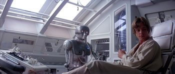 Movie still from “Star Wars: Episode V - The Empire Strikes Back” (1980), directed by Irvin Kershner – A man is sitting next to an iron man robot; Medium shot, High angle