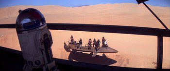 Movie still from “Star Wars: Episode VI - Return of the Jedi” (1983), directed by Richard Marquand – A group of people sitting on top of a boat in the desert; Extreme Wide shot, High angle