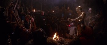 Movie still from “Star Wars: Episode VI - Return of the Jedi” (1983), directed by Richard Marquand – A group of people sitting around a fire pit; Wide shot, Over the shoulder angle