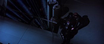 Movie still from “Star Wars: Episode VI - Return of the Jedi” (1983), directed by Richard Marquand – A man in a black suit standing next to pipes in a dark room; Wide shot, Overhead angle