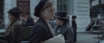 Movie still from “Suffragette” (2015), directed by Sarah Gavron – A woman in a hat and a jacket walking down a street; Medium shot, Over the shoulder angle