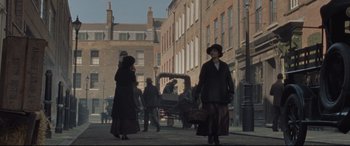 Movie still from “Suffragette” (2015), directed by Sarah Gavron – A woman in a long coat and hat walking down a street; Wide shot, High angle