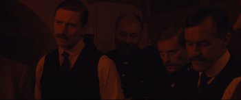 Movie still from “Suffragette” (2015), directed by Sarah Gavron – A group of men standing next to each other in the dark; Medium shot, Over the shoulder angle
