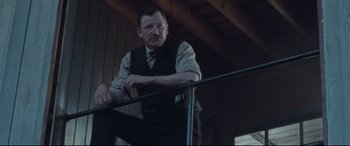Movie still from “Suffragette” (2015), directed by Sarah Gavron – A man leaning on a railing in front of a building; Medium shot, Low angle