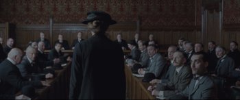 Movie still from “Suffragette” (2015), directed by Sarah Gavron – A woman in a black hat stands in front of a group of people; Wide shot, Over the shoulder angle