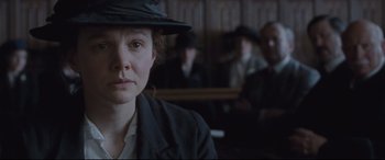 Movie still from “Suffragette” (2015), directed by Sarah Gavron – A woman wearing a black hat in front of a group of people; Close Up shot, Over the shoulder angle