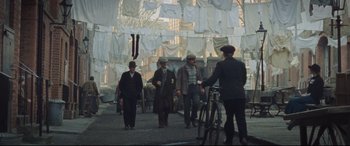 Movie still from “Suffragette” (2015), directed by Sarah Gavron – A group of men standing next to a bicycle; Wide shot, High angle