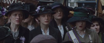 Movie still from “Suffragette” (2015), directed by Sarah Gavron – Two young women in hats and jackets are standing in a crowd of people; Close Up shot, Low angle