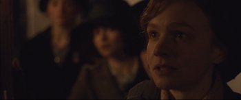 Movie still from “Suffragette” (2015), directed by Sarah Gavron – A woman is looking at the camera while a man in a black hat is in the background; Close Up shot, Over the shoulder angle