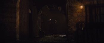 Movie still from “Suffragette” (2015), directed by Sarah Gavron – A person holding an open umbrella in a dark room; Extreme Wide shot, Over the shoulder angle