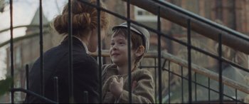 Movie still from “Suffragette” (2015), directed by Sarah Gavron – A young boy wearing a hat is looking through a fence; Close Up shot, Over the shoulder angle