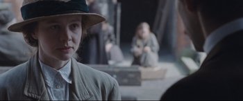 Movie still from “Suffragette” (2015), directed by Sarah Gavron – A woman wearing a hat standing in front of other people; Medium shot, Over the shoulder angle