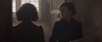 Movie still from “Suffragette” (2015), directed by Sarah Gavron – Two women standing next to each other in a dark room; Medium shot, Over the shoulder angle
