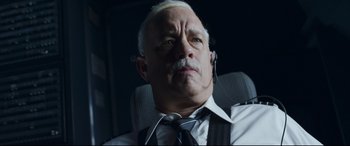 Movie still from “Sully” (2016), directed by Clint Eastwood – An older man wearing a tie and a headset; Close Up shot, Low angle