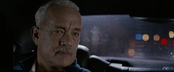 Movie still from “Sully” (2016), directed by Clint Eastwood – An older man sitting in the back seat of a car; Close Up shot, Over the shoulder angle