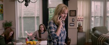Movie still from “Sully” (2016), directed by Clint Eastwood – A woman talking on a cell phone while another woman sits at a table in the background; Medium shot, Over the shoulder angle