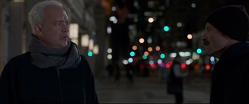 Movie still from “Sully” (2016), directed by Clint Eastwood – A man standing on a sidewalk at night with lights in the background; Close Up shot, Over the shoulder angle