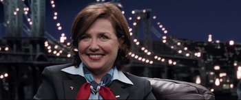 Movie still from “Sully” (2016), directed by Clint Eastwood – A woman wearing a suit and tie smiling for the camera; Medium shot, Over the shoulder angle