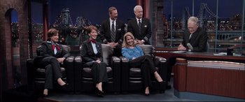 Movie still from “Sully” (2016), directed by Clint Eastwood – A group of people sitting on top of a black couch; Wide shot, High angle