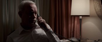 Movie still from “Sully” (2016), directed by Clint Eastwood – An older man talking on a phone while sitting in a chair; Close Up shot, High angle