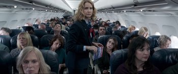 Movie still from “Sully” (2016), directed by Clint Eastwood – A woman is standing on an airplane holding a book; Medium shot, Over the shoulder angle