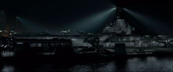 Movie still from “Sully” (2016), directed by Clint Eastwood – A large aircraft carrier in the dark with a light shining on it; Extreme Wide shot, High angle