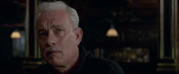 Movie still from “Sully” (2016), directed by Clint Eastwood – An older man sitting in a chair looking into the distance; Close Up shot, Over the shoulder angle