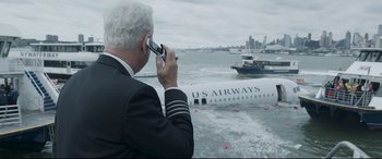 Movie still from “Sully” (2016), directed by Clint Eastwood – A man in a suit is on a cell phone in front of an airplane; Medium shot, High angle