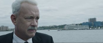 Movie still from “Sully” (2016), directed by Clint Eastwood – An older man in a suit and tie looking off into the distance in front of a body of water; Close Up shot, Over the shoulder angle