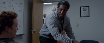 Movie still from “Sully” (2016), directed by Clint Eastwood – A man in a gray jacket is leaning on a door; Medium shot, Over the shoulder angle