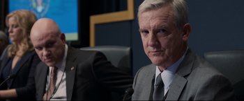 Movie still from “Sully” (2016), directed by Clint Eastwood – An older man wearing a suit and tie sitting in a chair; Close Up shot, Over the shoulder angle