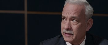 Movie still from “Sully” (2016), directed by Clint Eastwood – An older man in a black suit and white beard; Close Up shot, Over the shoulder angle