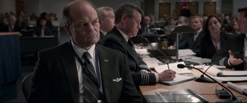 Movie still from “Sully” (2016), directed by Clint Eastwood – A group of men sitting at a conference room table; Medium shot, Over the shoulder angle