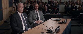 Movie still from “Sully” (2016), directed by Clint Eastwood – A man sitting at a table in front of an audience; Medium shot, Over the shoulder angle