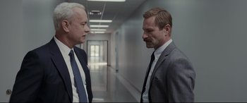 Movie still from “Sully” (2016), directed by Clint Eastwood – Two men in business suits are standing in a hallway; Medium shot, Over the shoulder angle
