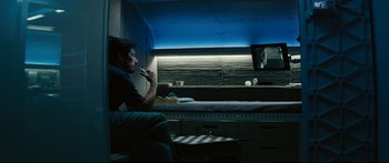 Movie still from “Sunshine” (2007), directed by Danny Boyle – A man sitting in front of a tv in a room; Medium shot, Over the shoulder angle