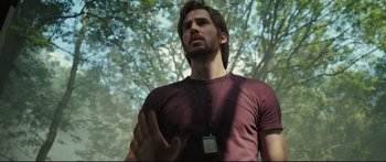 Movie still from “Sunshine” (2007), directed by Danny Boyle – A man in a maroon t - shirt is standing in front of a tree; Medium shot, Low angle
