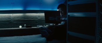 Movie still from “Sunshine” (2007), directed by Danny Boyle – A man sitting in front of a computer on a bed; Wide shot, High angle