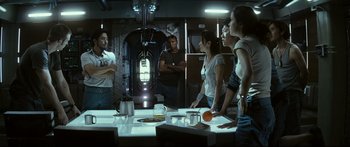 Movie still from “Sunshine” (2007), directed by Danny Boyle – A group of people standing around a table in a room; Medium shot, Over the shoulder angle