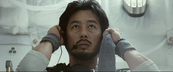 Movie still from “Sunshine” (2007), directed by Danny Boyle – A man with a headset is holding his hands up; Close Up shot, Low angle