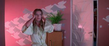 Movie still from “Suspiria” (1977), directed by Dario Argento – A young woman standing in front of a mirror in front of a plant; Medium shot, Low angle