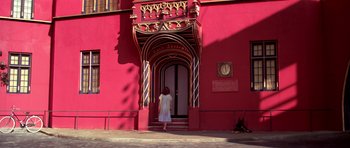 Movie still from “Suspiria” (1977), directed by Dario Argento – A woman standing in front of a red building; Wide shot, Low angle