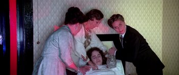 Movie still from “Suspiria” (1977), directed by Dario Argento – A woman is laying in a hospital bed while two other women look on; Medium shot, High angle