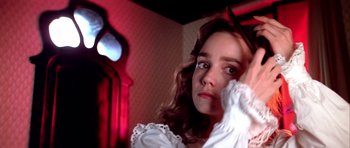 Movie still from “Suspiria” (1977), directed by Dario Argento – A young woman in a white dress looking at the camera; Close Up shot, Over the shoulder angle