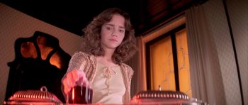 Movie still from “Suspiria” (1977), directed by Dario Argento – A woman sitting at a table in front of a candle; Close Up shot, High angle