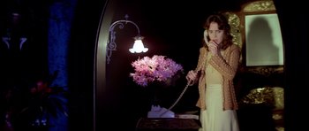 Movie still from “Suspiria” (1977), directed by Dario Argento – A woman talking on a phone next to flowers; Medium shot, Low angle