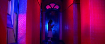 Movie still from “Suspiria” (1977), directed by Dario Argento – A woman standing in front of a door in a dark room; Wide shot, Low angle