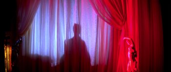 Movie still from “Suspiria” (1977), directed by Dario Argento – A man sitting in front of a window with red curtains; Wide shot, Low angle